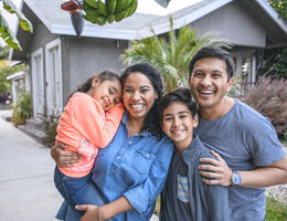 A woman, man and two kids pose, smiling, in front of a house.