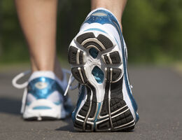 Sole of a sneaker as a woman walks down a path.